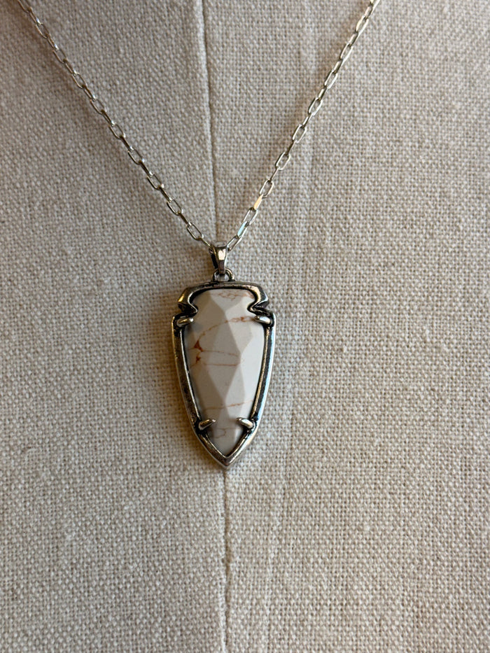 Arrowhead pendant necklace close-up: gold-tone frame with white faceted stone