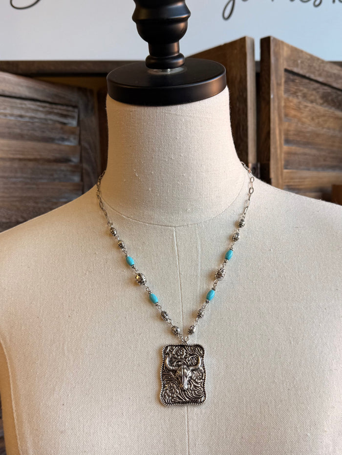 Pendant necklace with ornate cowskull medallion, silver chain, and turquoise beads