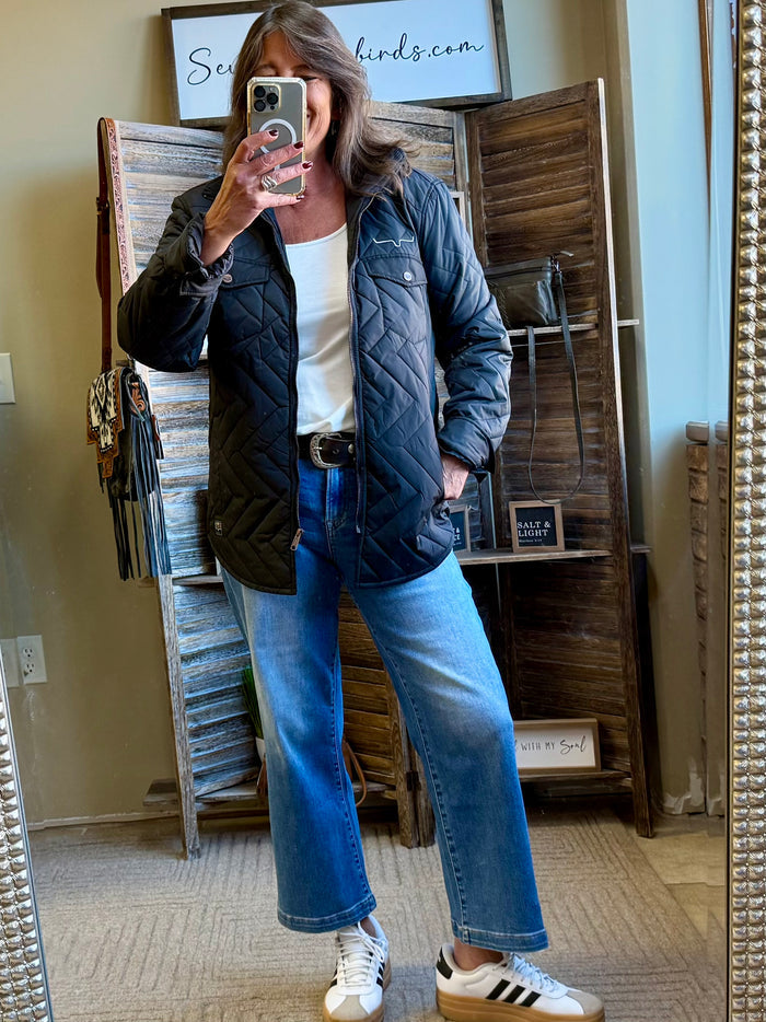 Dark quilted coat with zip front and snap pockets, styled with jeans and sneakers