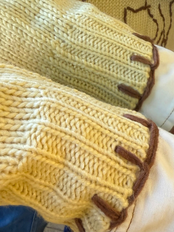 Mustard knit sweater hem close-up with brown ribbed trim and visible cable stitching