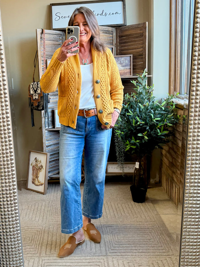 Mustard cable-knit cotton cardigan worn over jeans, front buttons visible