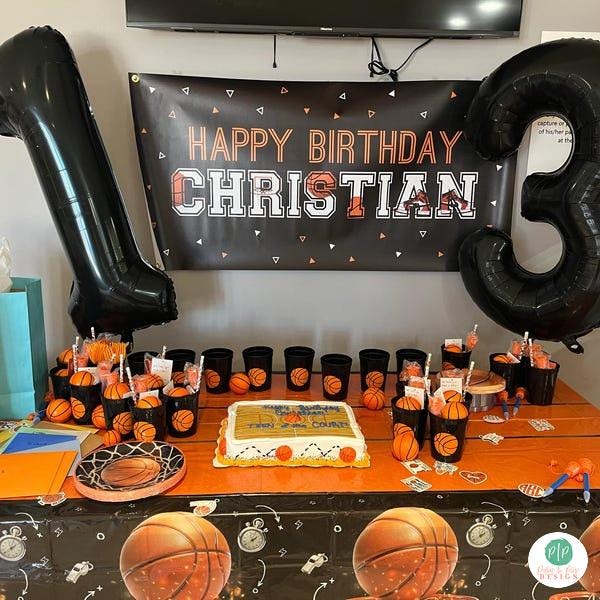 A birthday party setup with a banner that reads "Happy Birthday Christian", a cake, balloons, and basketball-themed decorations.