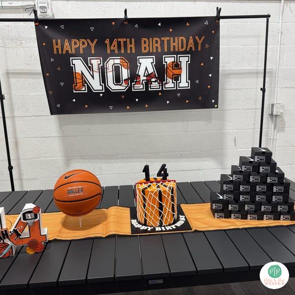a birthday celebration setup with a banner that reads "Happy 14th Birthday Noah", a basketball, and a cake with the number 14 on it.