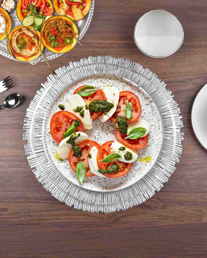 Round woven metallic table mat with concentric circular fringe, silver tone under plate
