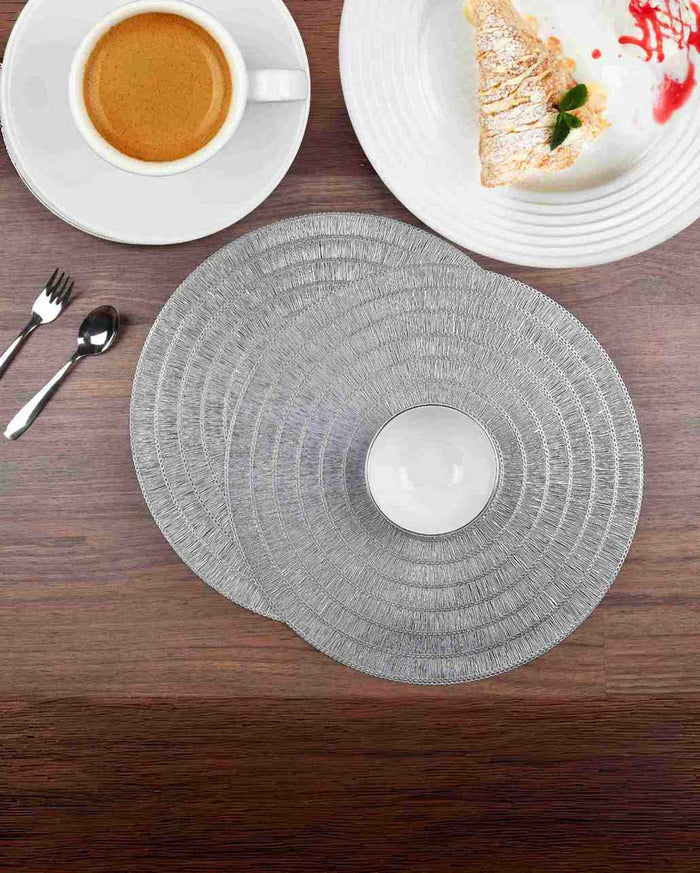 Round silver textured placemat on a wooden table with cups and plates