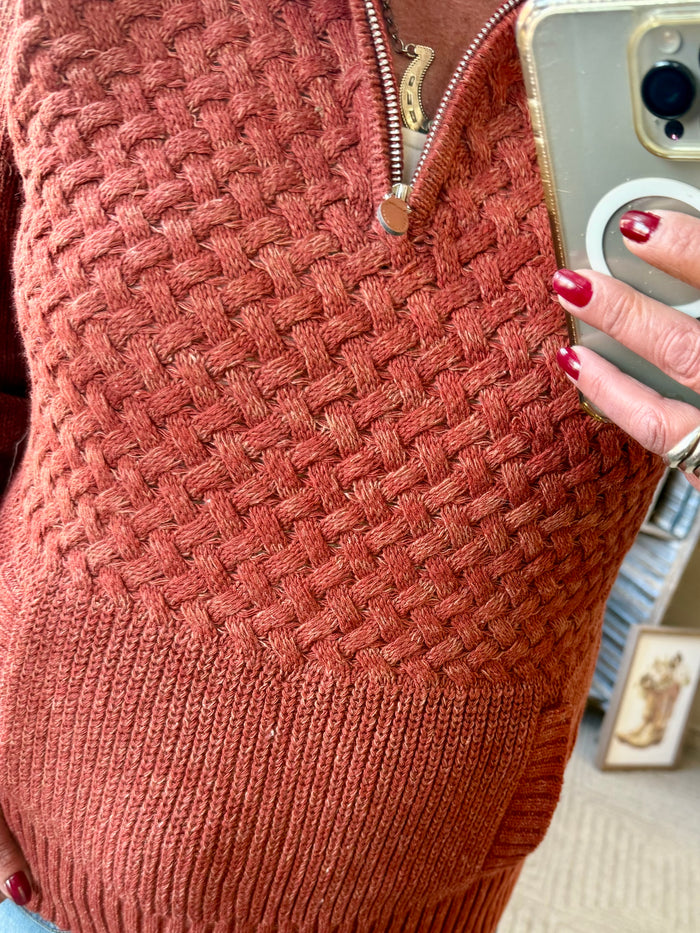 Rust cable-knit quarter-zip sweater close-up with front pocket and zipper