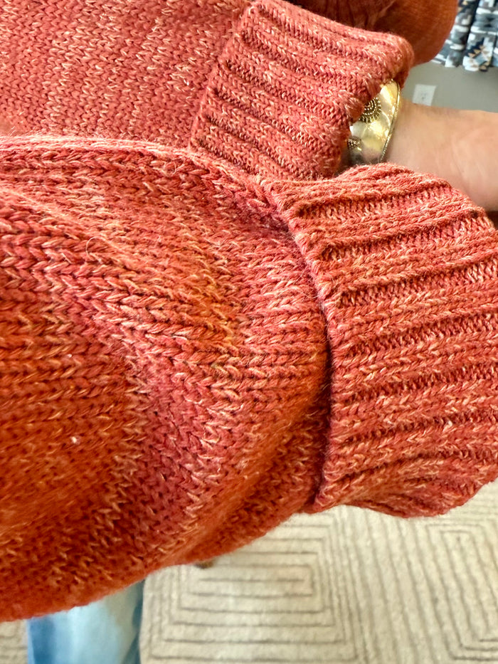 Rust cable-knit sweater close-up with braided texture and half-zip collar