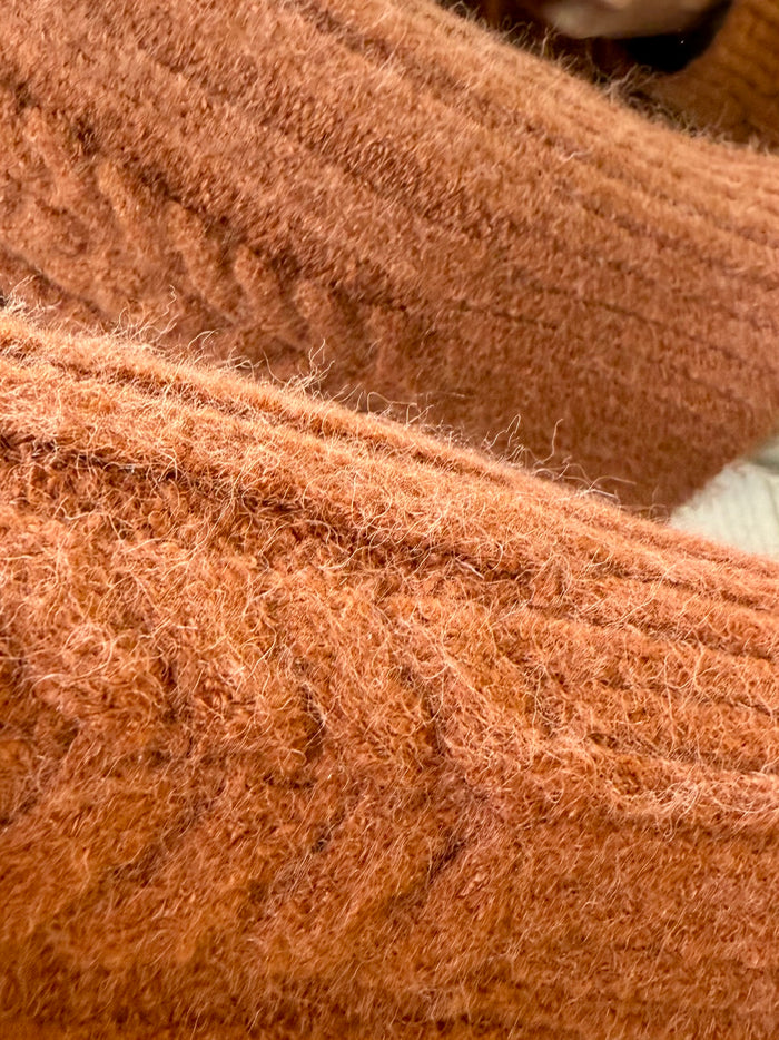 Rust cable knit sweater fabric close-up with textured pattern