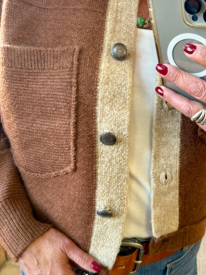 Rust-brown cardigan front with cream placket, metal buttons, and textured knit cuffs