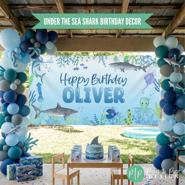 Boys Under the Sea Shark themed birthday party banner hung in backyard with balloon garland and shark themed desserts