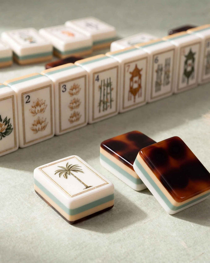 Mahjong tiles with illustrated faces; palm tree tile and tortoise-shell backs on surface.
