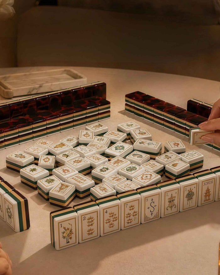 Mahjong tile set with illustrated faces and tortoise-shell backs, stacked on table.